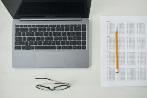 Flat lay of a laptop, online exam sheet, and pencil on a white desk, perfect for education and technology themes.